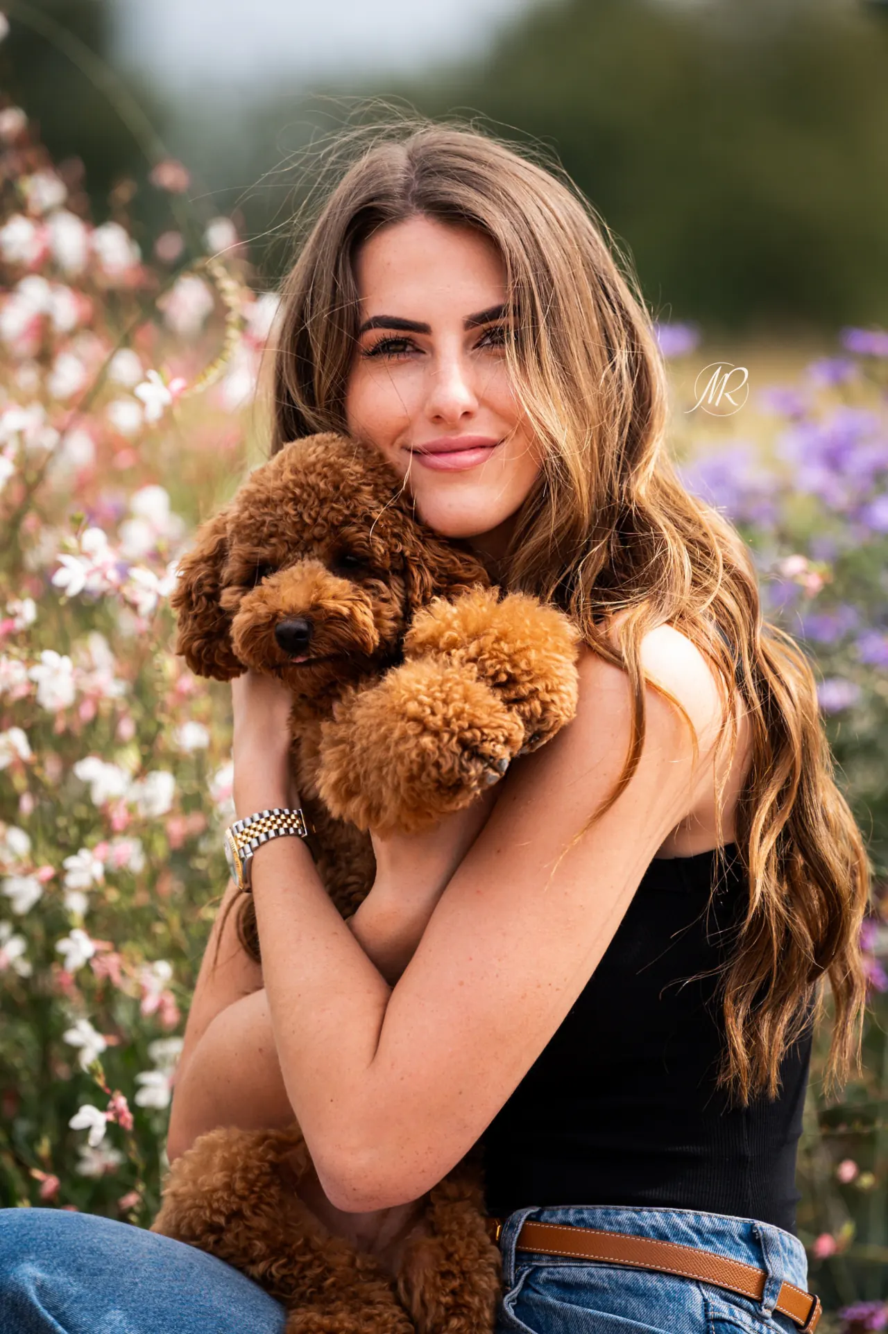 Jonge vrouw knuffelt een rode toypoodle tussen de bloemen
