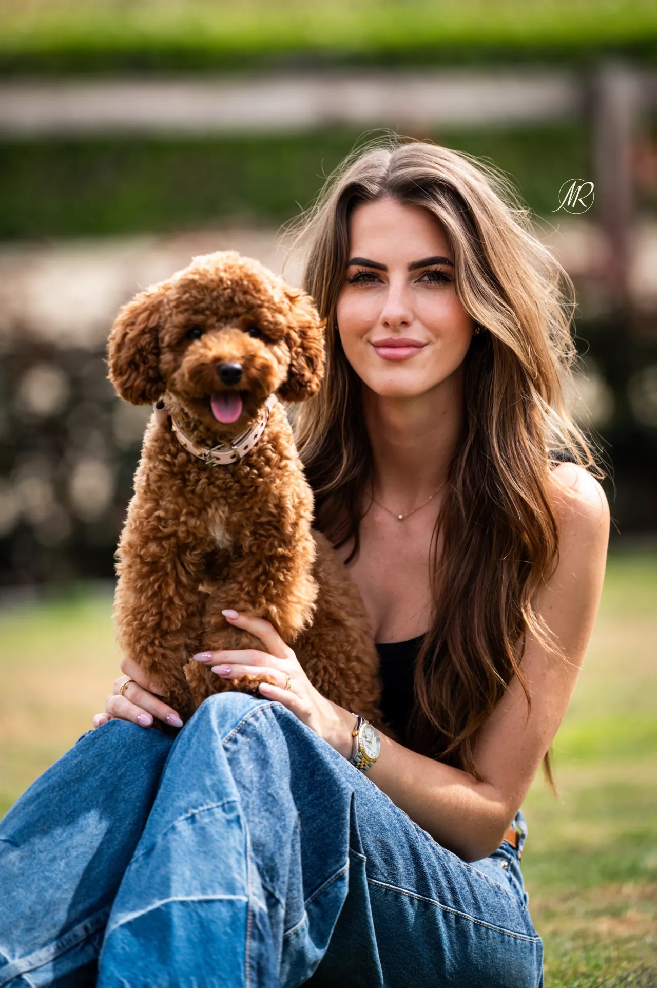 Jonge vrouw zit in het gras met een rode toypoodle